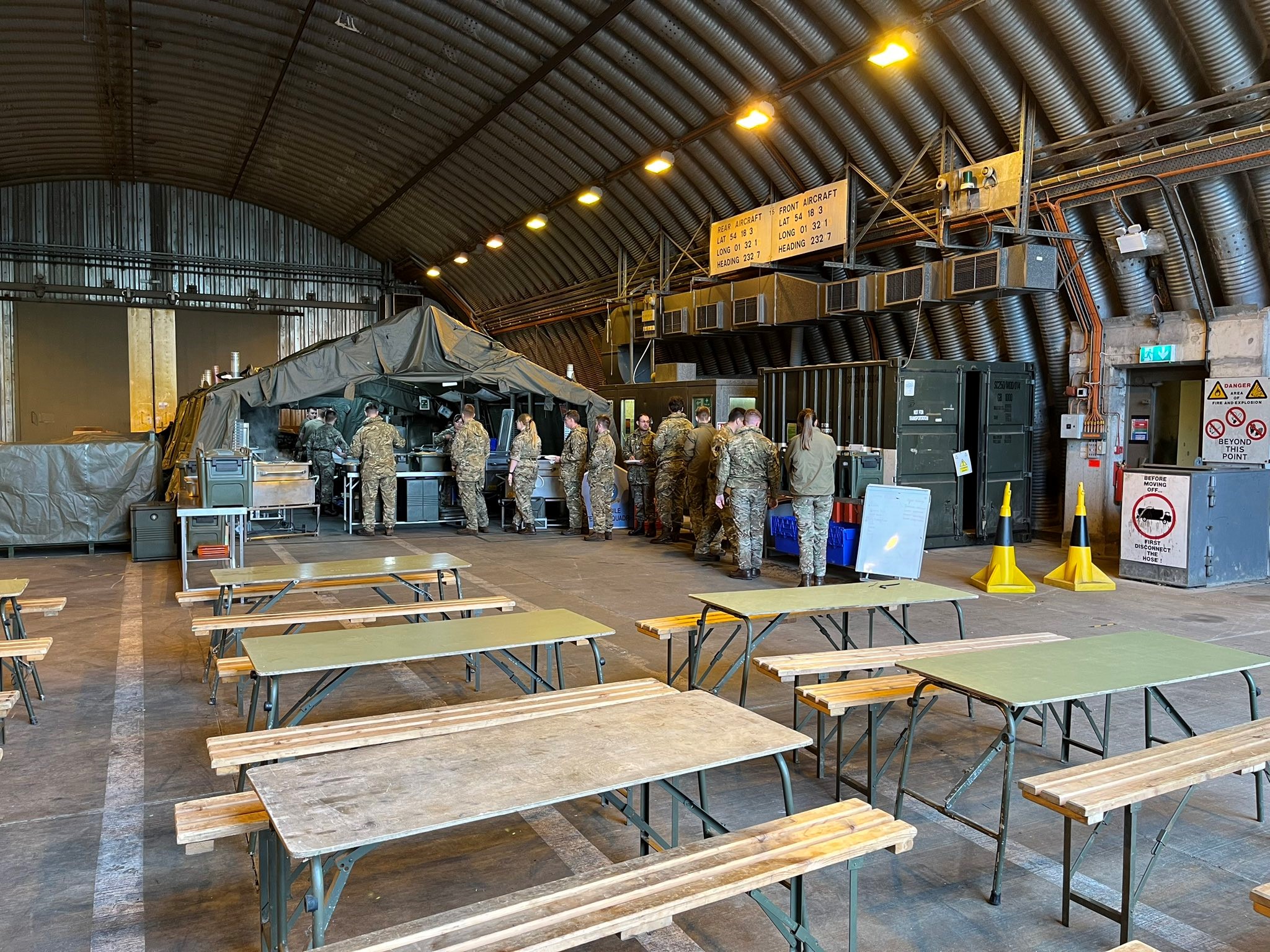 Photo - Personnel queue for a meal from a tented field kitchen, erected within a hardened shelter.